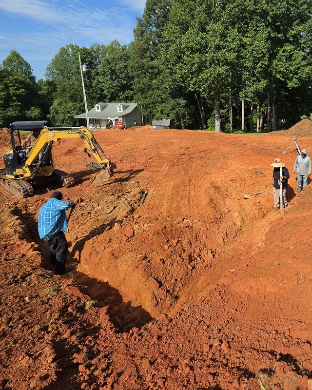 Premier crew grading a building pad in red clay with a mini excavator and a laser level