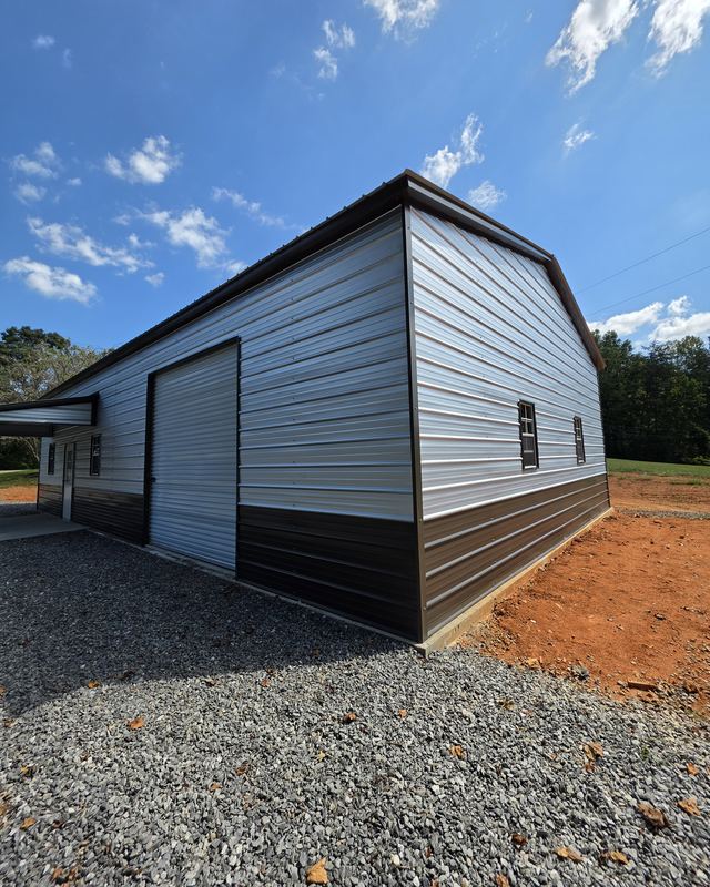 Finished two-tone metal garage with a roll-up door and windows on a new concrete slab